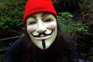 Individual wearing a Guy Fawkes mask and a red knit hat outdoors.