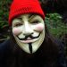 Individual wearing a Guy Fawkes mask and a red knit hat outdoors.