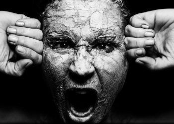 A person screaming with cracked clay on face, conveying intense emotion.