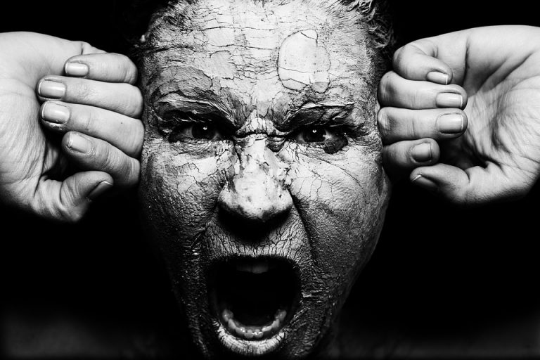 A person screaming with cracked clay on face, conveying intense emotion.