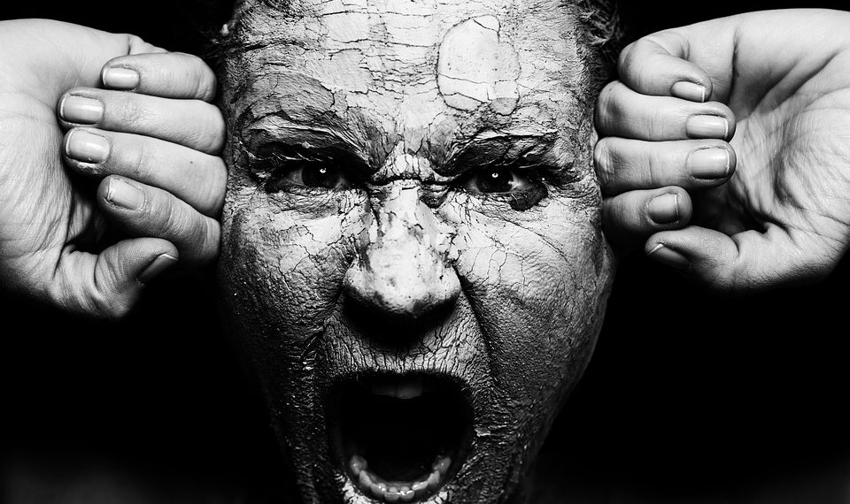 A person screaming with cracked clay on face, conveying intense emotion.