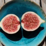 Halved figs in a blue bowl on a wooden table.