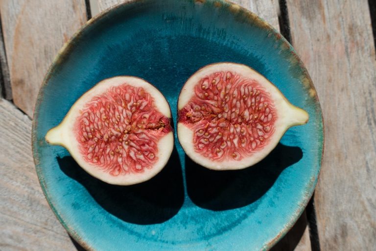 Halved figs in a blue bowl on a wooden table.
