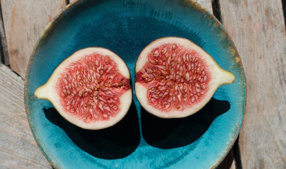Halved figs in a blue bowl on a wooden table.
