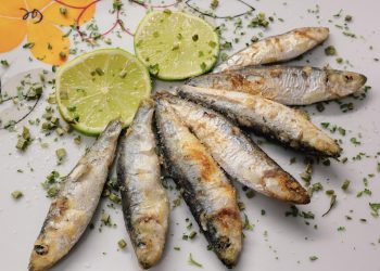 Grilled sardines garnished with lime slices and herbs.