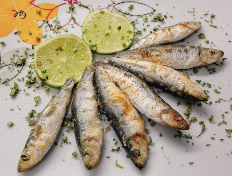Grilled sardines garnished with lime slices and herbs.