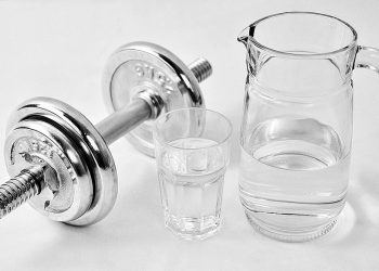 Dumbbell beside a jug and glass of water, promoting fitness balance.