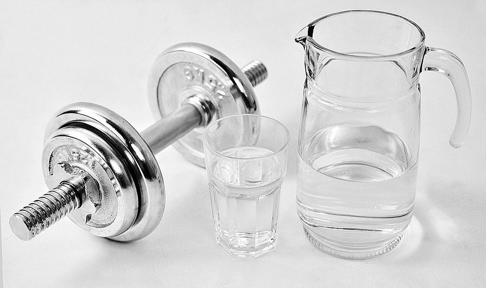 Dumbbell beside a jug and glass of water, promoting fitness balance.