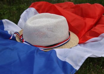 Straw hat with French flag ribbon on a tricolor flag laid on grass.
