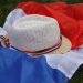 Straw hat with French flag ribbon on a tricolor flag laid on grass.