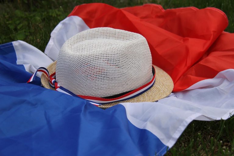 Straw hat with French flag ribbon on a tricolor flag laid on grass.