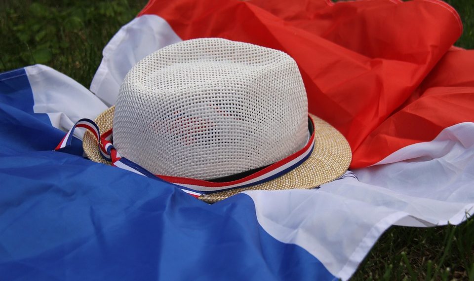 Straw hat with French flag ribbon on a tricolor flag laid on grass.