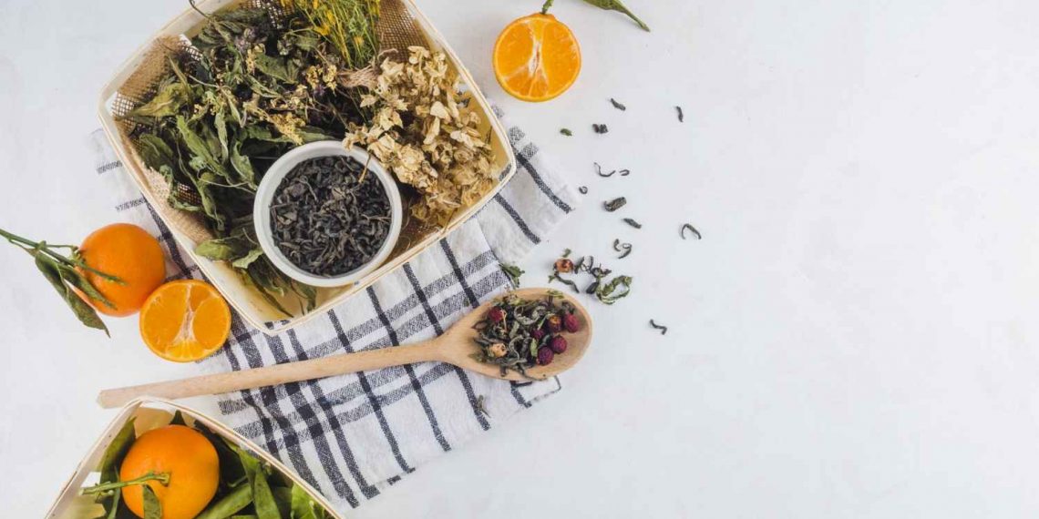 Dried herbs and fresh citrus on a checkered cloth, alongside green tea leaves.