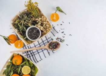 Dried herbs and fresh citrus on a checkered cloth, alongside green tea leaves.