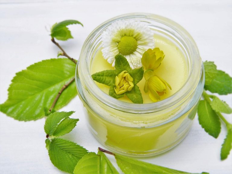 Herbal salve in a jar with fresh flowers and leaves.
