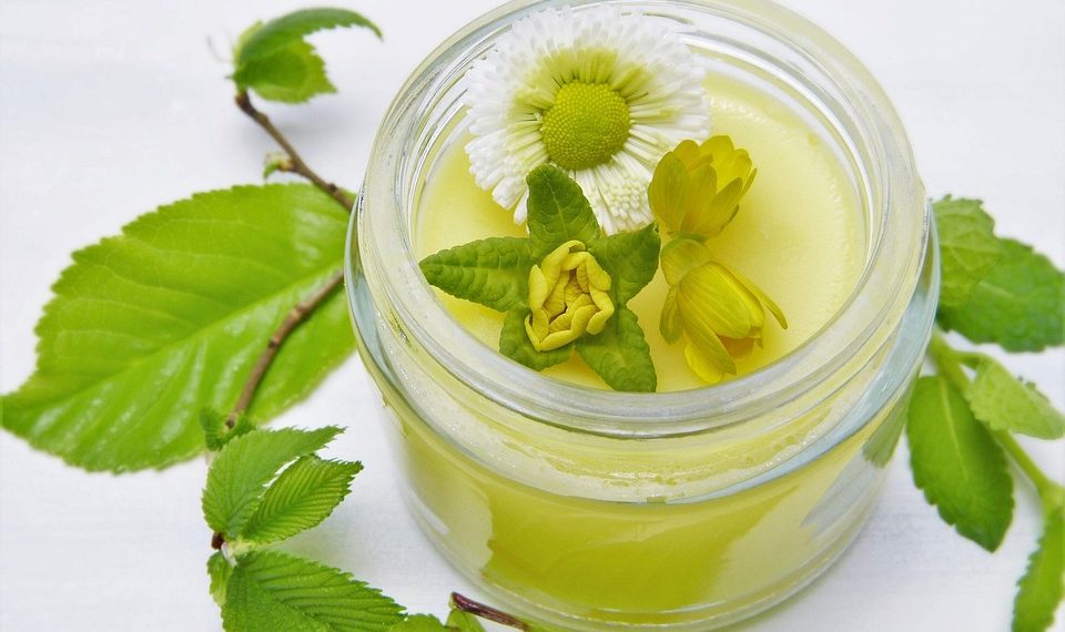 Herbal salve in a jar with fresh flowers and leaves.