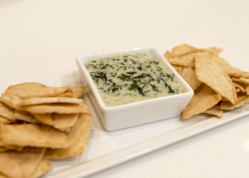 Creamy spinach dip with pita chips on a platter.