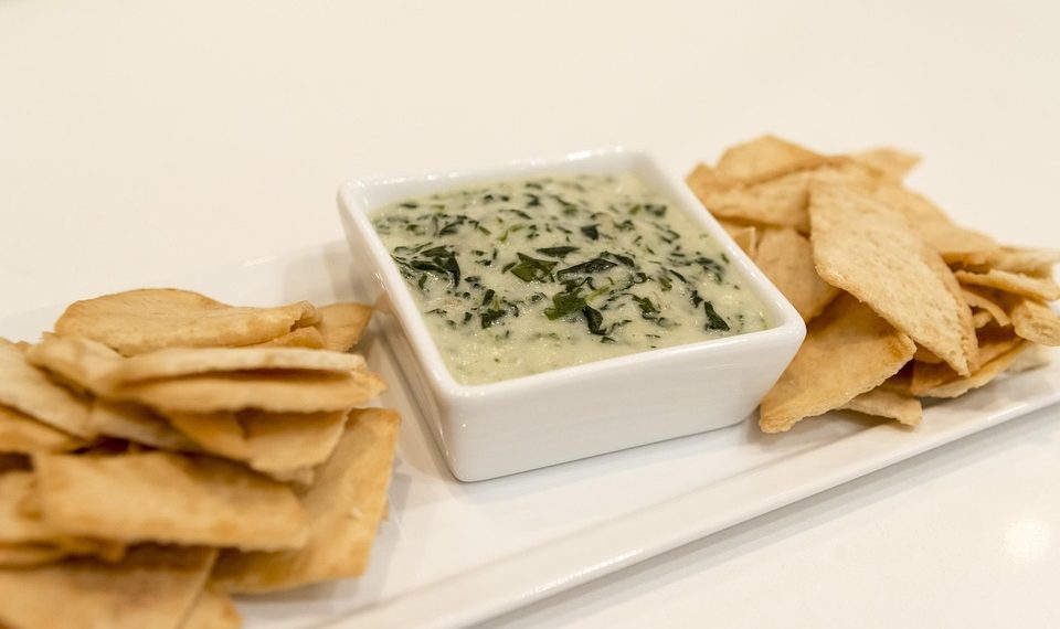 Creamy spinach dip with pita chips on a platter.