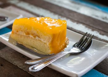 Slice of mango cake with cream on a plate with utensils.