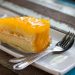 Slice of mango cake with cream on a plate with utensils.