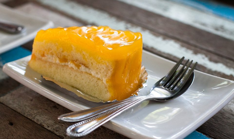 Slice of mango cake with cream on a plate with utensils.