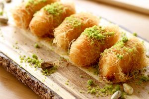 Golden pastries topped with pistachios on a rustic wooden board.