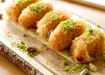Golden pastries topped with pistachios on a rustic wooden board.