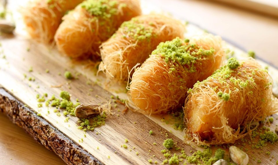 Golden pastries topped with pistachios on a rustic wooden board.