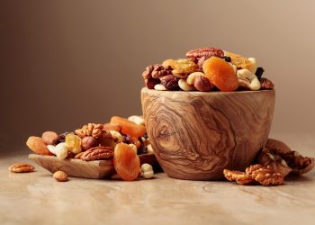 Bowl of mixed nuts and dried fruits on a wooden table.