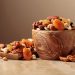 Bowl of mixed nuts and dried fruits on a wooden table.