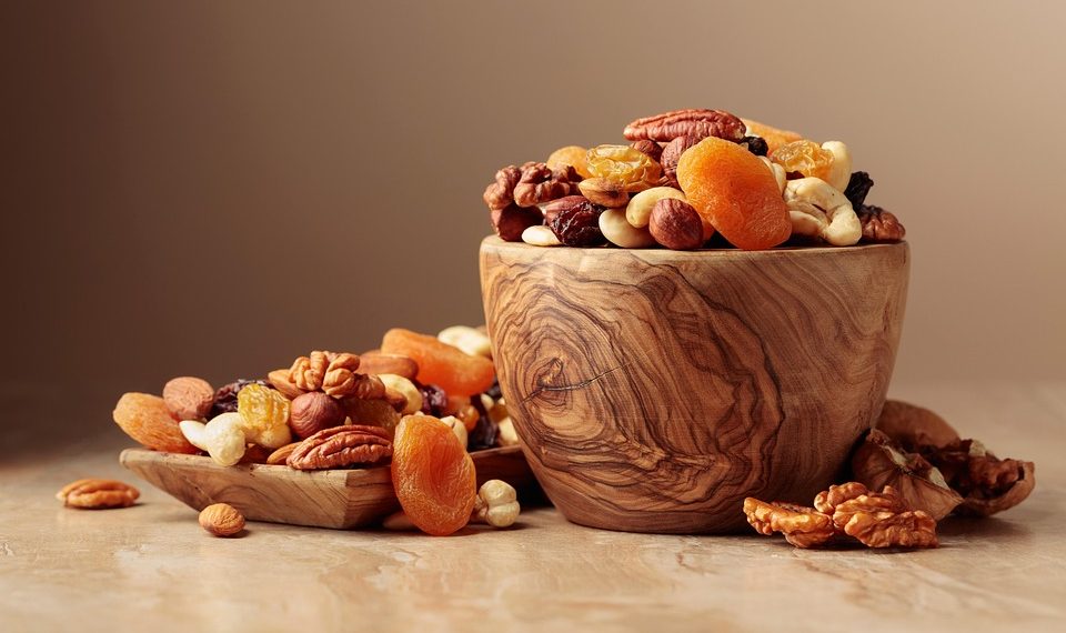 Bowl of mixed nuts and dried fruits on a wooden table.