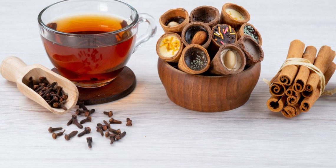 Tea with filled biscuit cups, cloves, and cinnamon sticks.