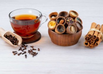 Tea with filled biscuit cups, cloves, and cinnamon sticks.