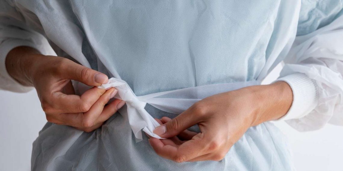 Tying the waist of a medical gown securely for protection.