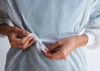 Tying the waist of a medical gown securely for protection.
