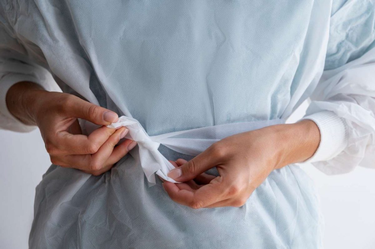 Tying the waist of a medical gown securely for protection.