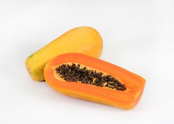Whole and sliced papaya with seeds on a white background.
