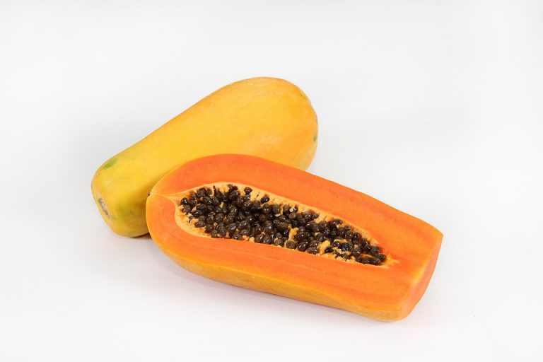 Whole and sliced papaya with seeds on a white background.