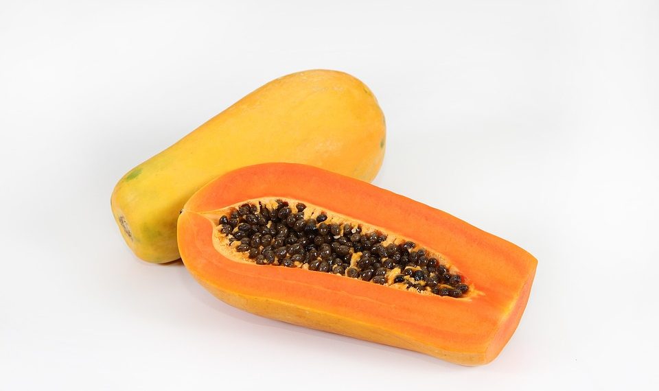 Whole and sliced papaya with seeds on a white background.