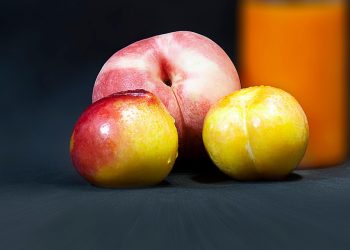 Ripe peaches and golden plums on a dark background nearby orange juice.
