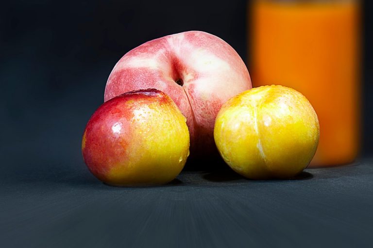 Ripe peaches and golden plums on a dark background nearby orange juice.
