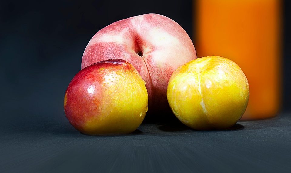 Ripe peaches and golden plums on a dark background nearby orange juice.