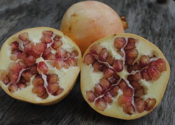 Halved pomegranates with red seeds on a wooden table.