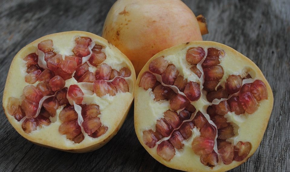 Halved pomegranates with red seeds on a wooden table.