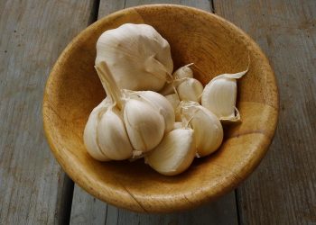 Garlic cloves in a wooden bowl on a rustic table.