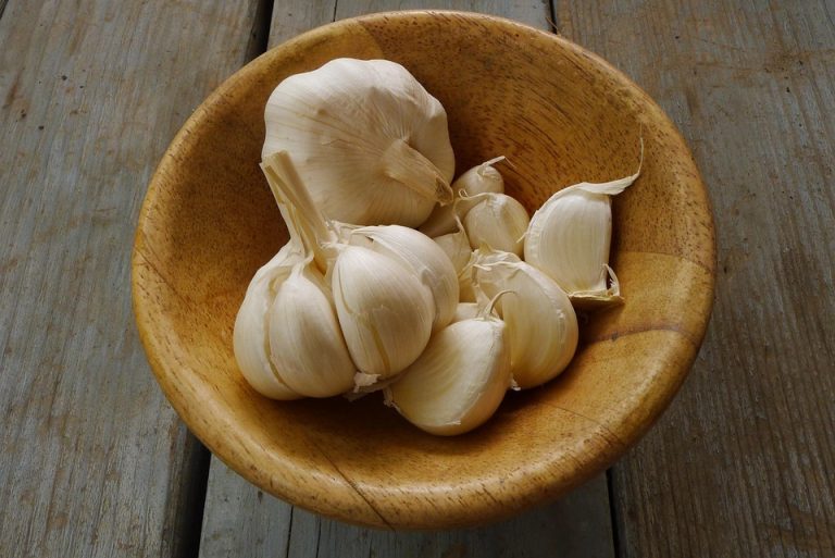 Garlic cloves in a wooden bowl on a rustic table.
