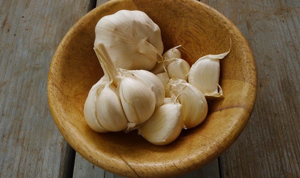 Garlic cloves in a wooden bowl on a rustic table.