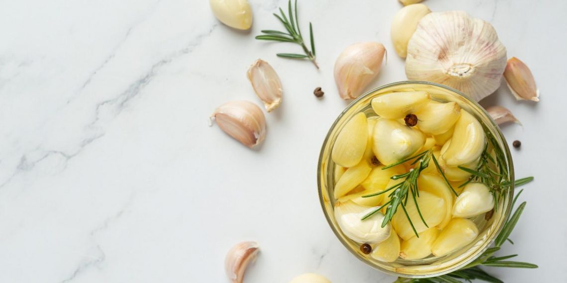 Garlic cloves with rosemary in a jar on marble background.