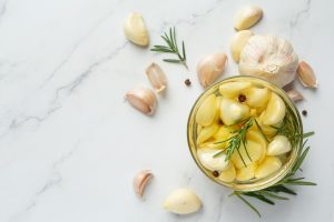 Garlic cloves with rosemary in a jar on marble background.