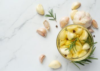 Garlic cloves with rosemary in a jar on marble background.